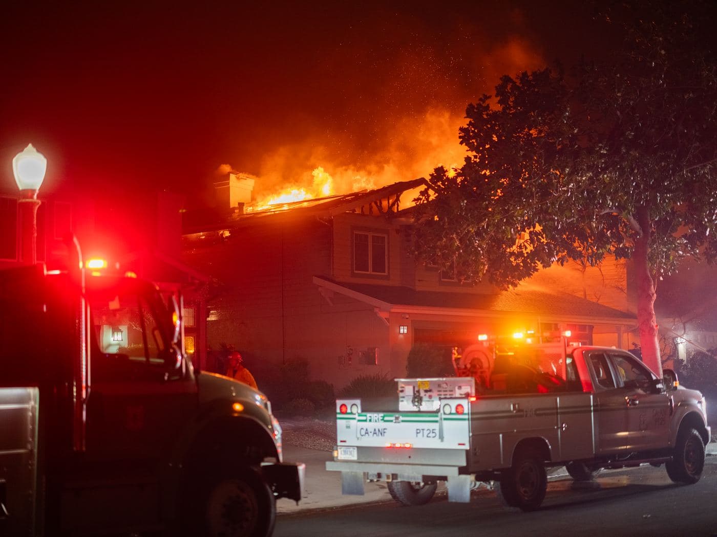 Fire engines on a residential street at night while a house burns.